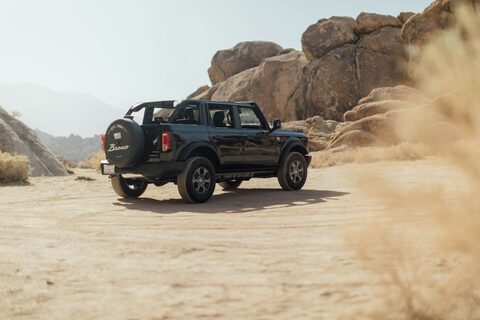 A black Ford Bronco kicking up dust off road