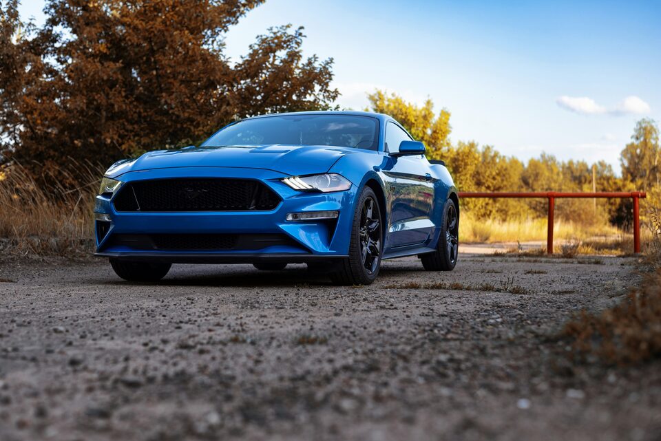A blue Ford Mustang parked on gravel