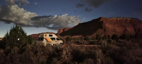 A camper parked below red desert cliffs