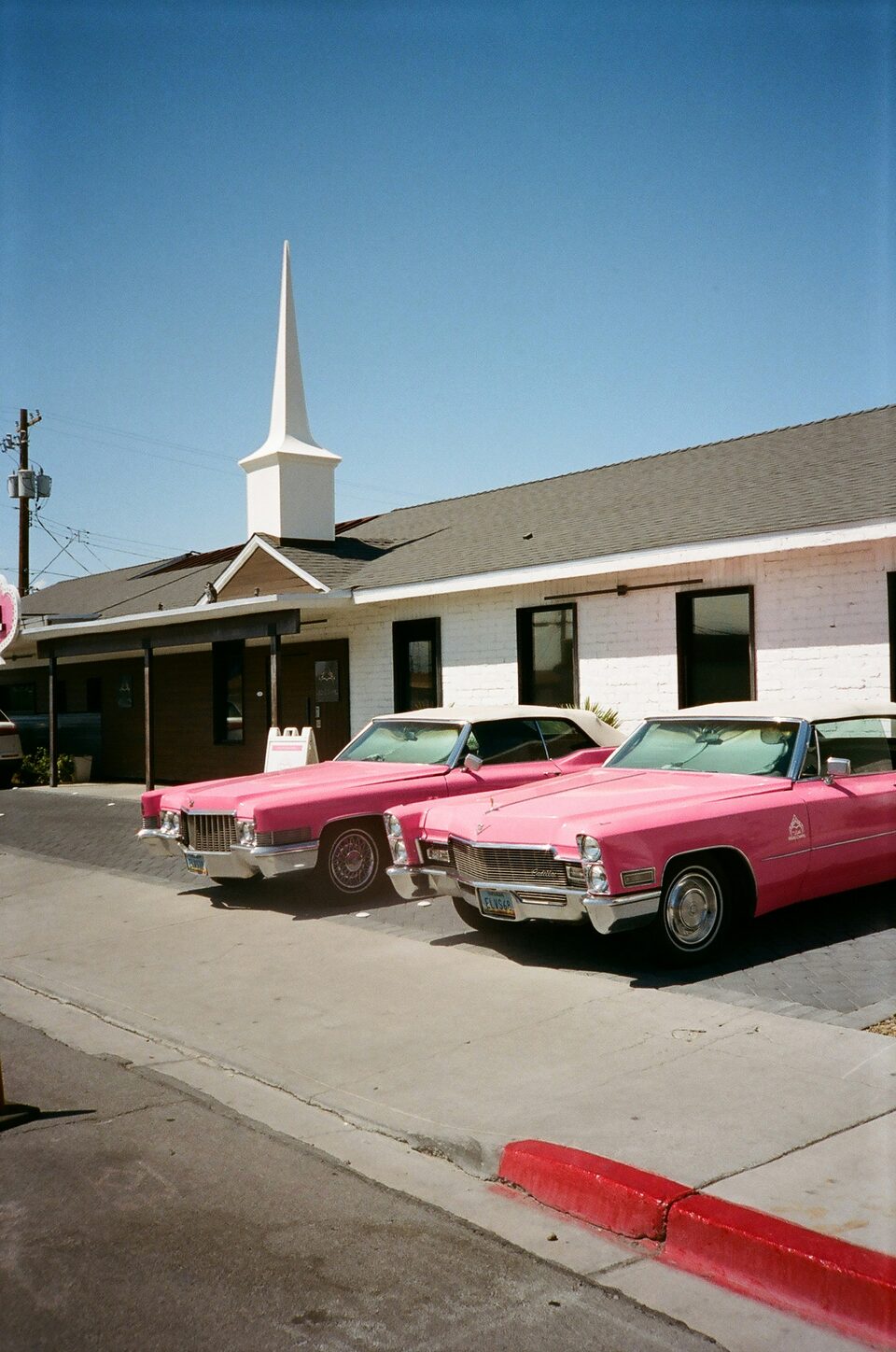 Two pink classic Cadillacs parked in front of a white chapel