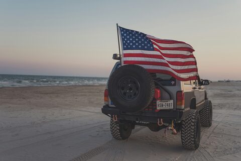 An off-road SUV on the sand with an American flag