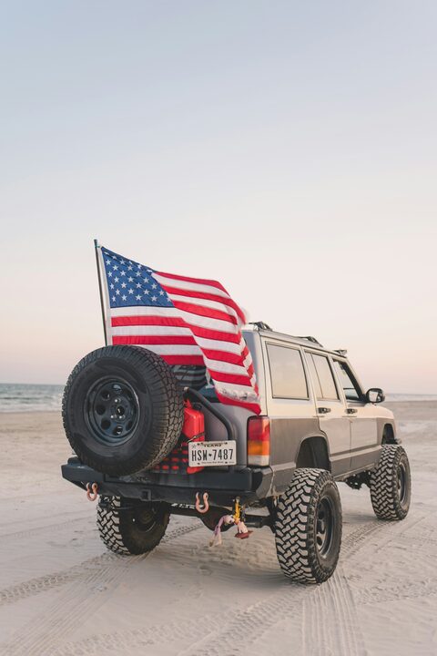 A Jeep Cherokee on the beach flying an American flag