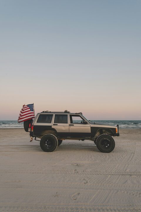 A Jeep Cherokee on a beach flying an American flag