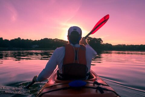 A kayaker paddling into a pink sunset