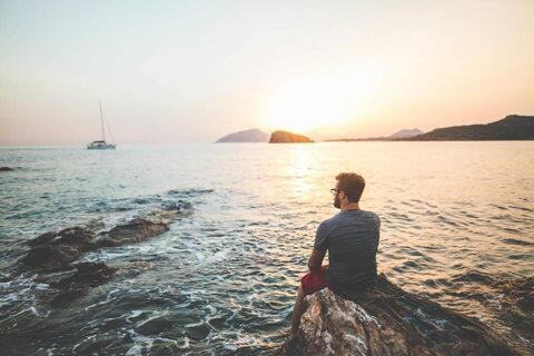 A man sitting by the sea at sunset