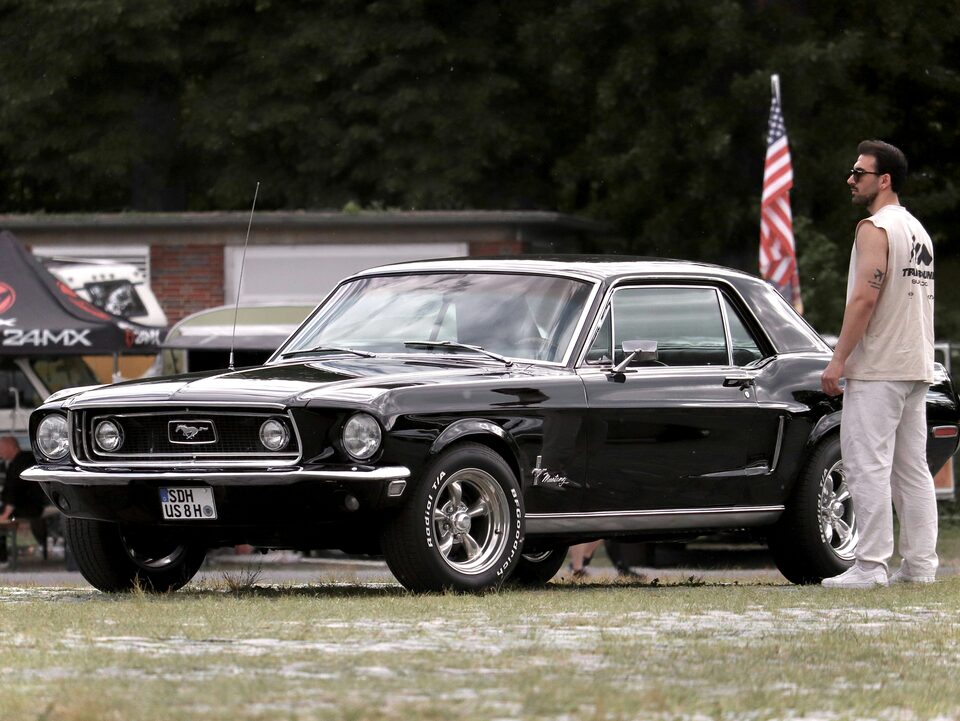 A black classic Ford Mustang on the grass with an American flag