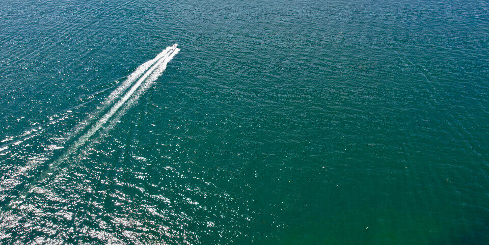 A speedboat crossing teal water seen from above