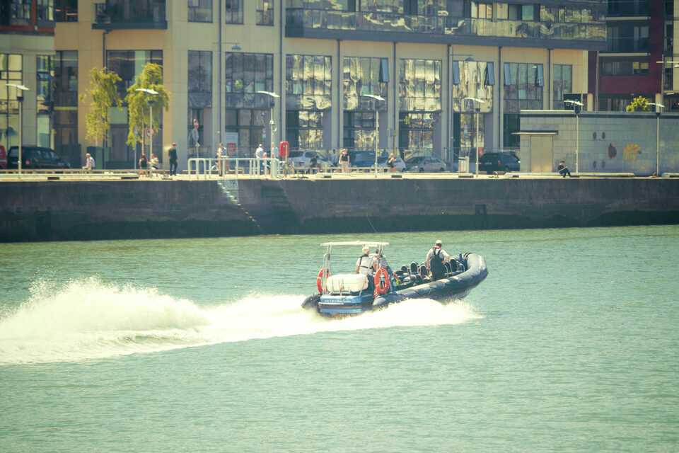 A rigid inflatable boat running along a harbor wall