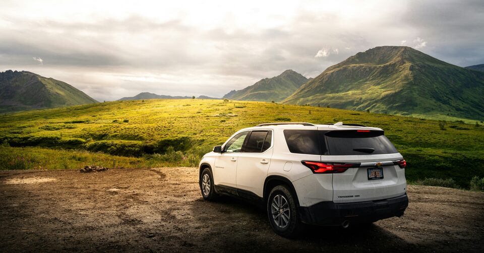 A white SUV parked below green mountains