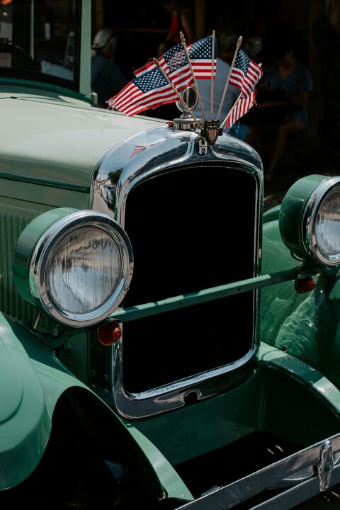 A vintage green car decorated with American flags