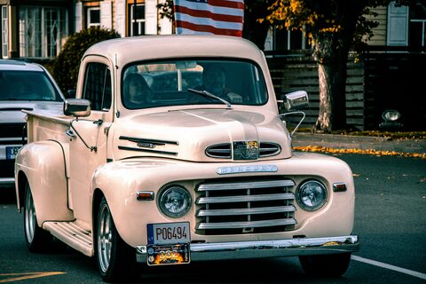 A cream classic pickup truck with an American flag behind it