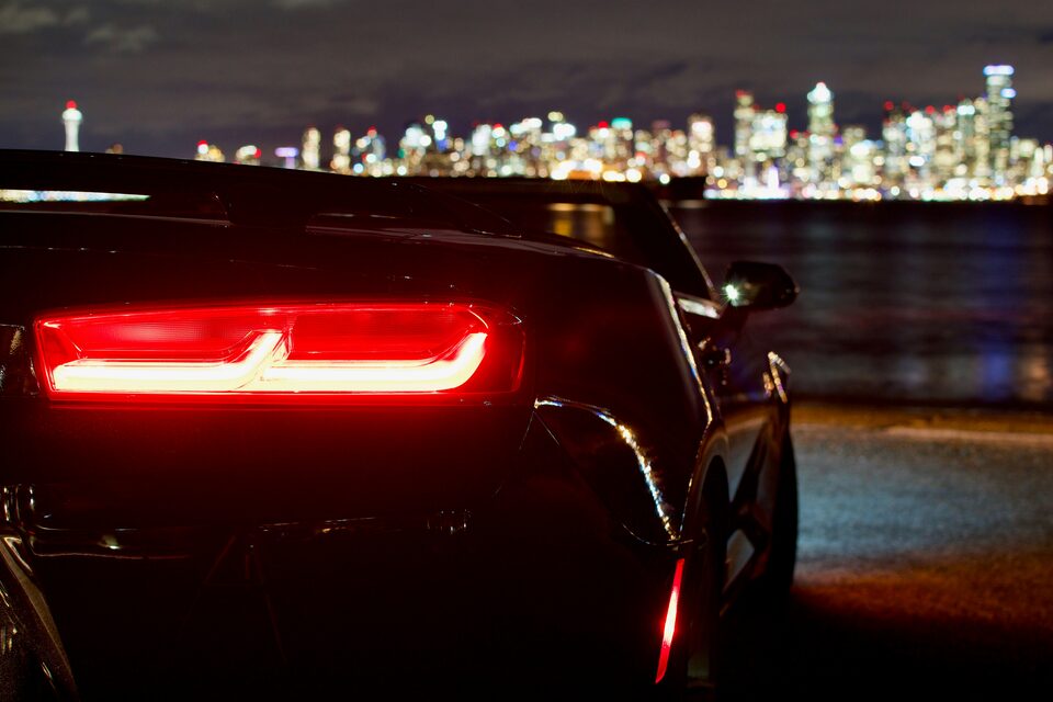 The glowing taillight of a sports car with a city skyline at night