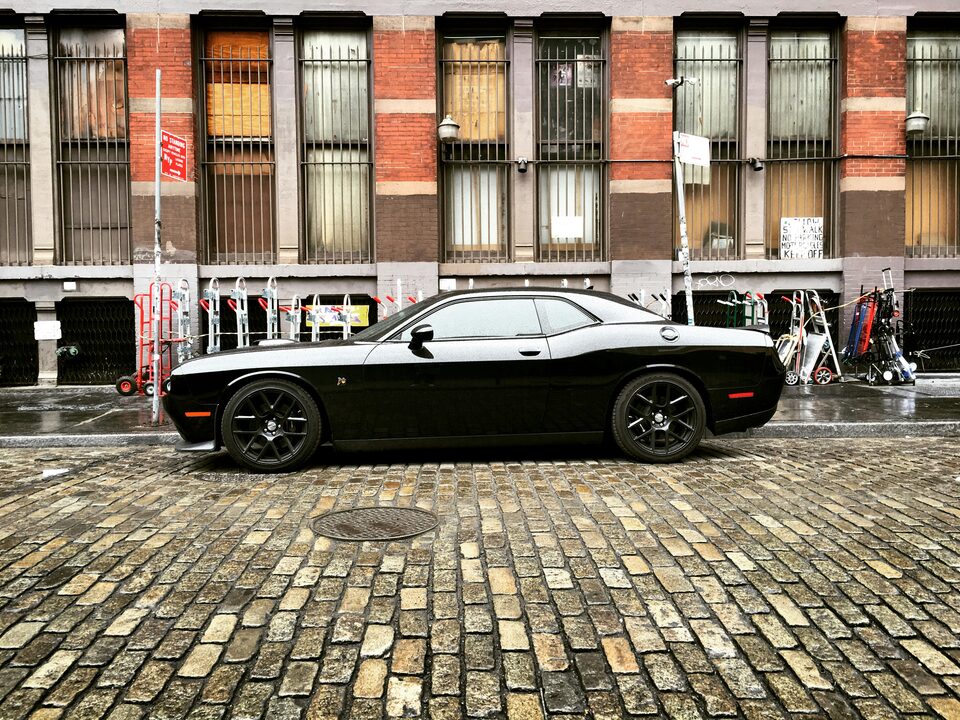 A black Dodge Challenger on a cobblestone street