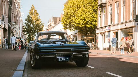 A blue classic Corvette on a tree lined street