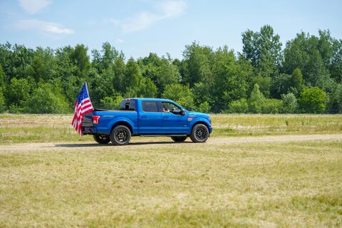 A blue pickup truck flying an American flag in a field