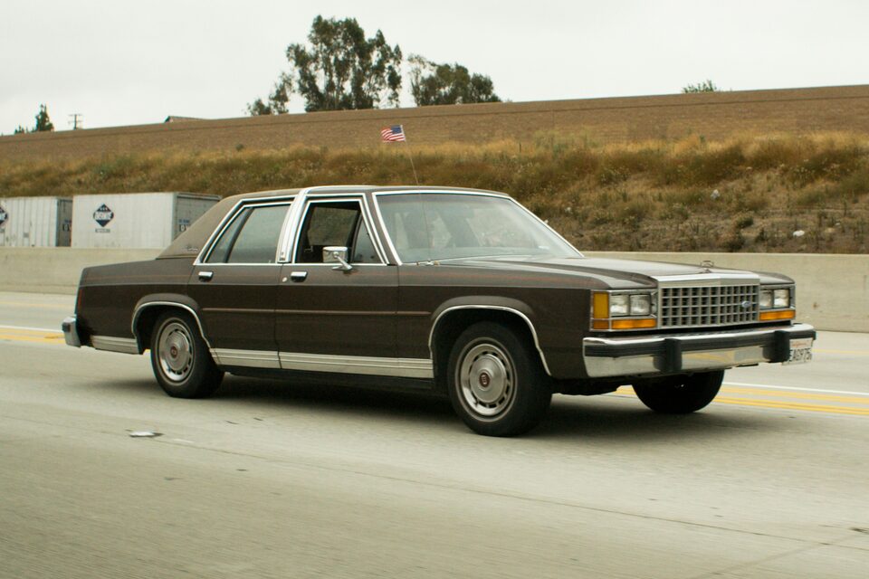 A brown classic sedan parked by a hillside