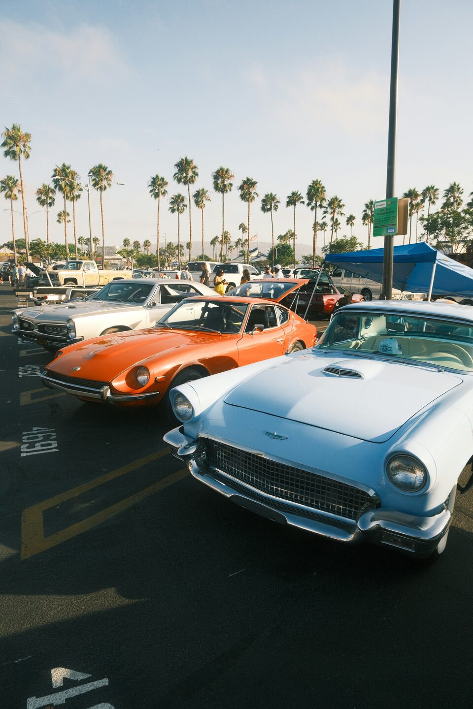 An orange classic sports car and a white Thunderbird at a show