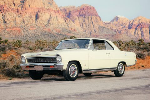 A cream classic Chevrolet Nova below red desert cliffs