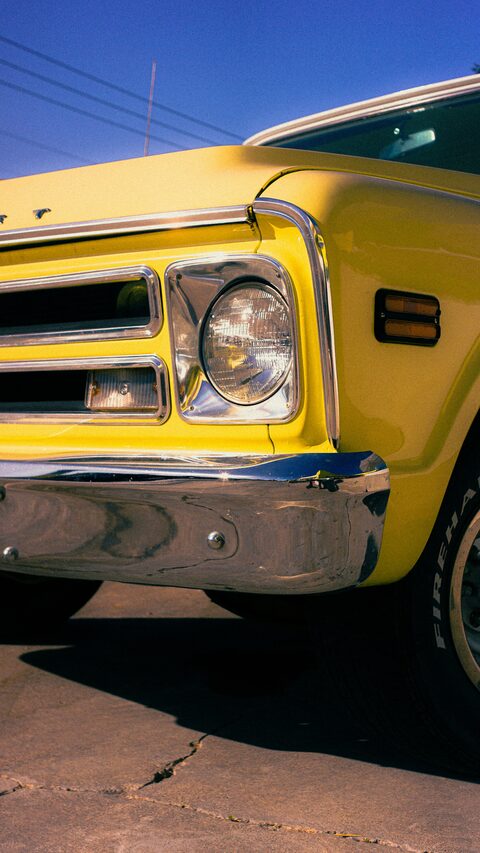The headlight and chrome bumper of a yellow classic car