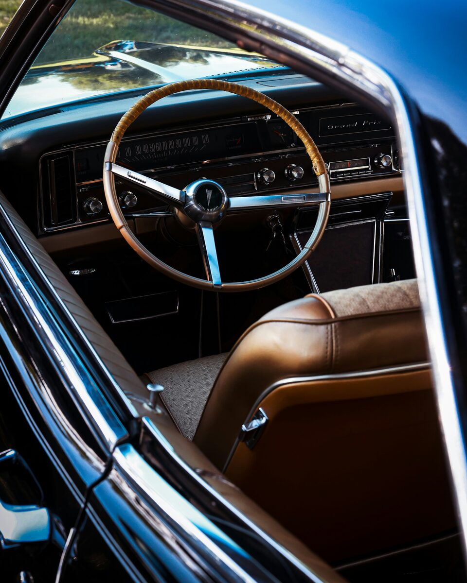 A classic car interior with a wood steering wheel and tan leather seats