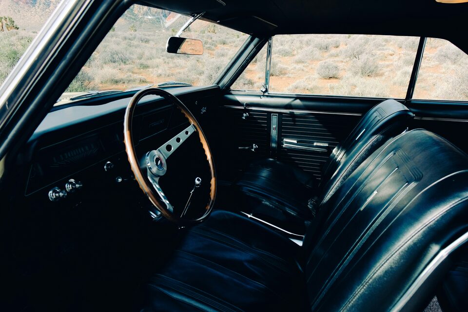 The black interior of a classic car with a wood steering wheel