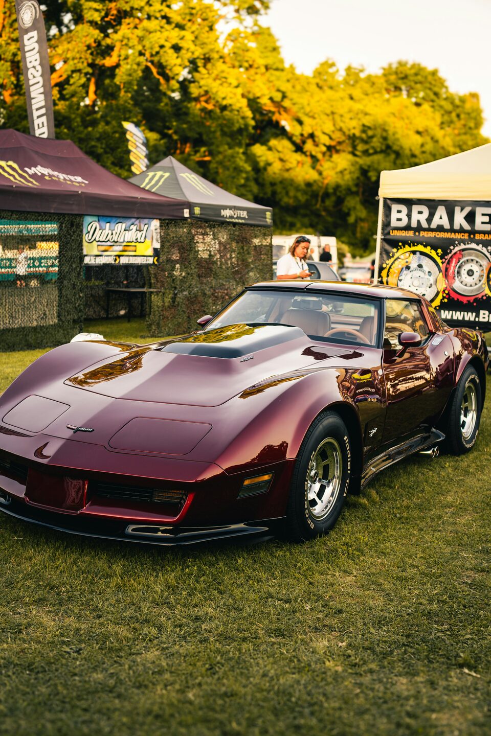 A maroon classic Corvette parked on the grass