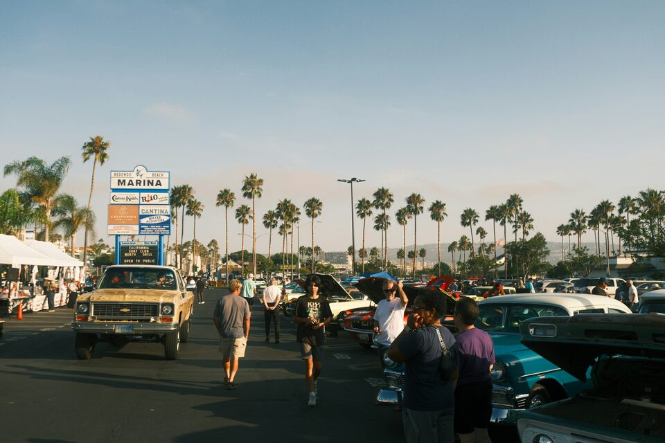 Shoppers walking a busy lot of cars under palm trees