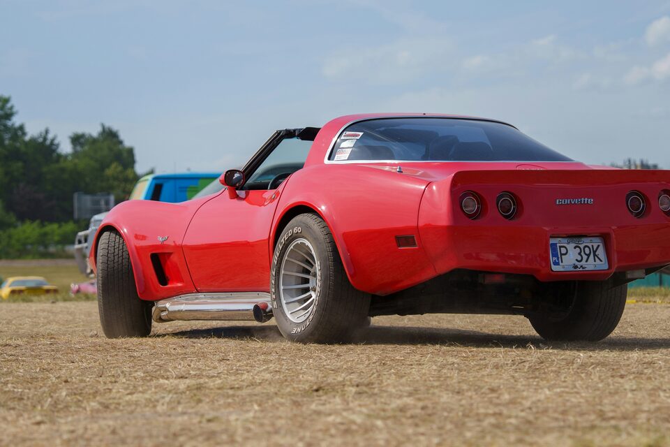 A red classic Corvette parked on a dirt lot