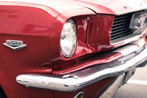 The headlight and chrome bumper of a red classic Ford Mustang