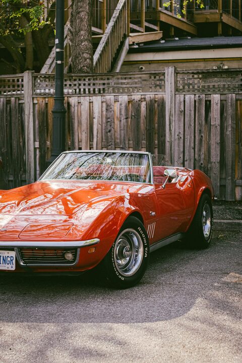 An orange classic Corvette convertible beside a wooden wall