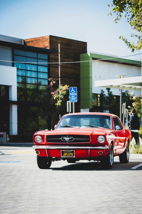 A red classic Mustang beside a modern building