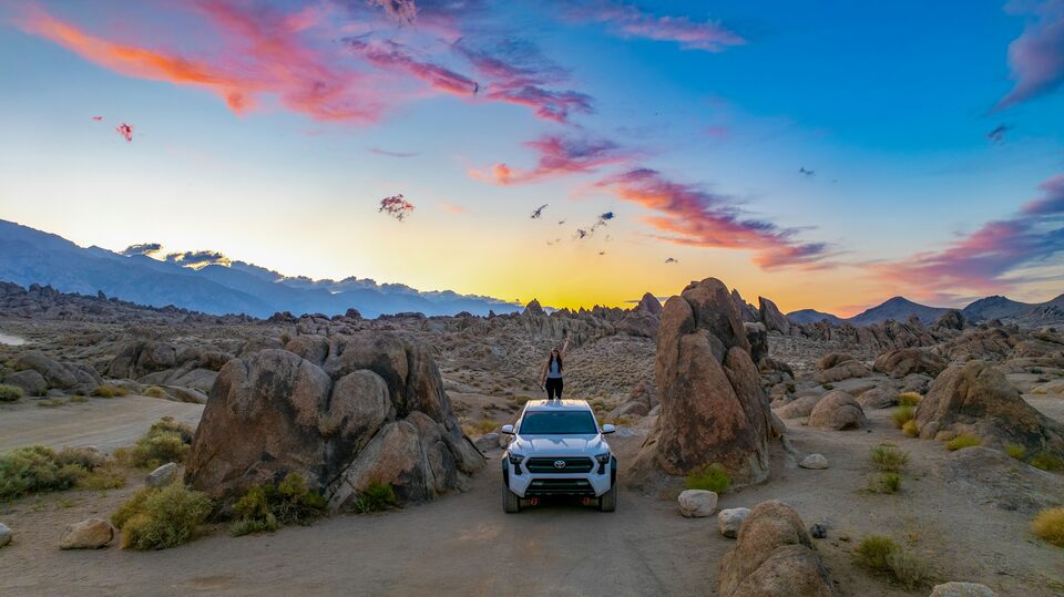 An SUV parked among desert rocks at sunset