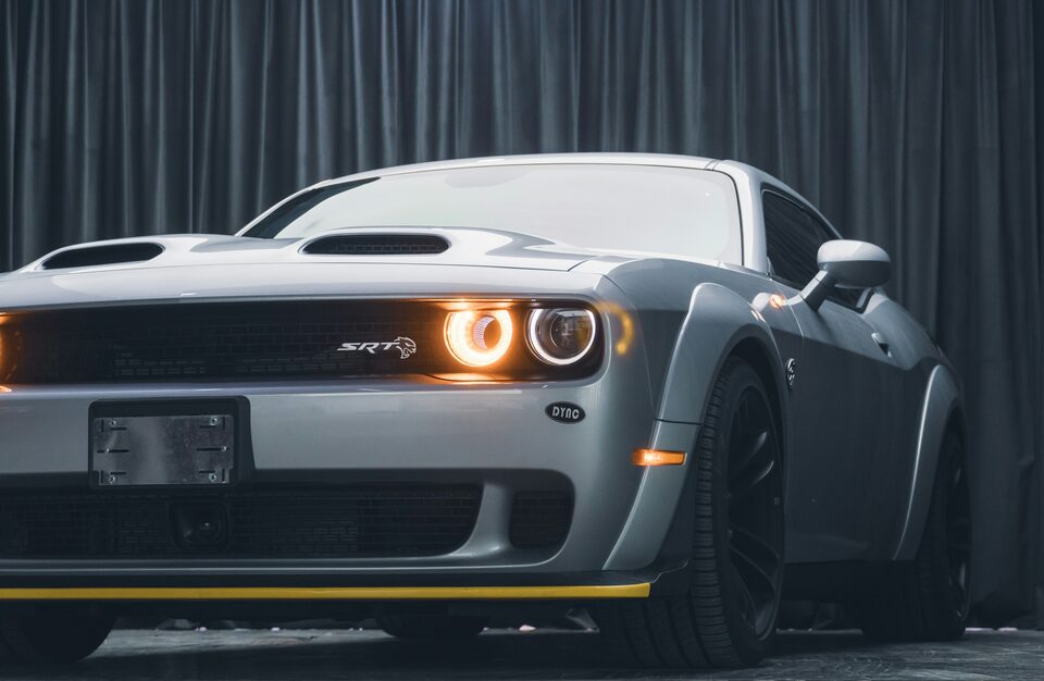 A gray Dodge Challenger with its headlights glowing