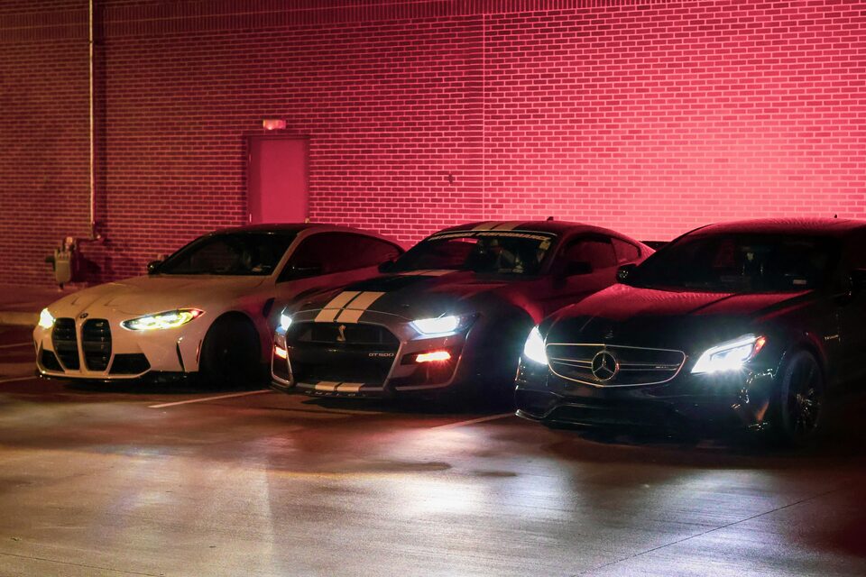 Three luxury sports cars lit up against a red wall at night