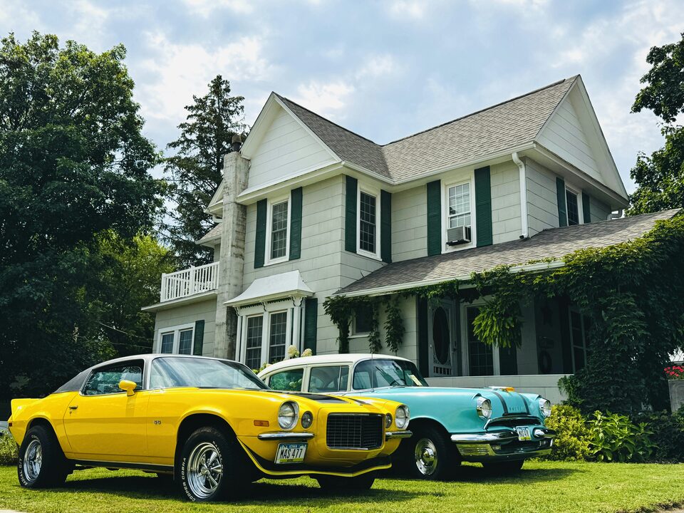 Yellow and teal classic cars on a lawn in front of a white house