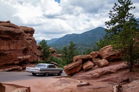 A classic car parked among red rocks and pine trees