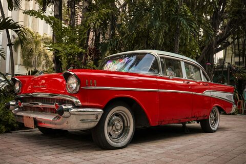 A red 1957 Chevrolet Bel Air parked under palm trees