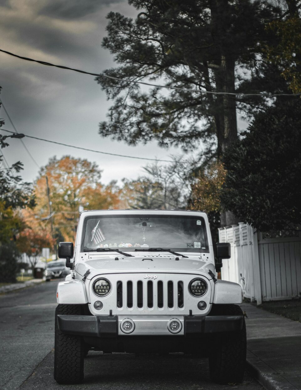 A white Jeep Wrangler under autumn trees