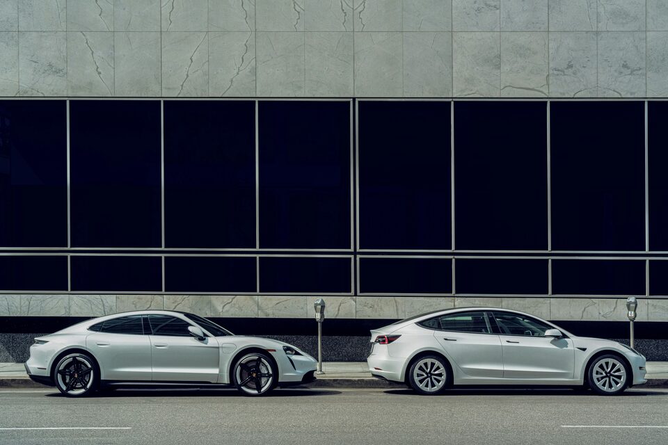 Two white electric cars parked along a glass building